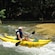 An adolescent outfitted in a life jacket and helmet navigates a single person kayak through mild white water waves